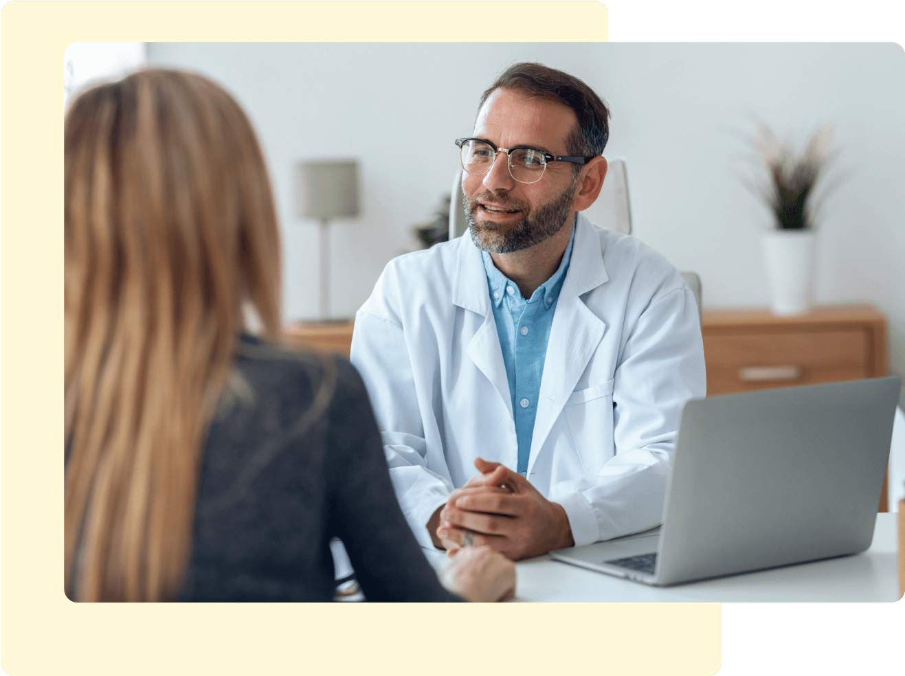 Male doctor with laptop speaking with female patient