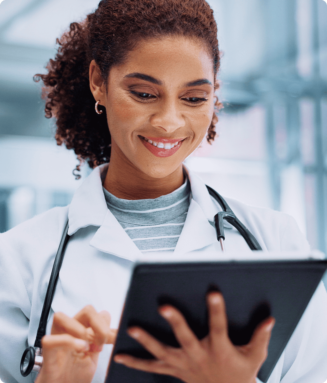 Young female doctor smiling while viewing patient charts on a tablet.